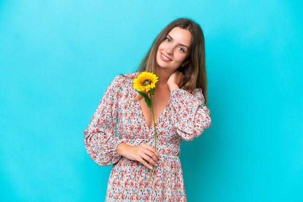 Jeune femme caucasienne tenant tournesol isolé sur fond bleu en riant