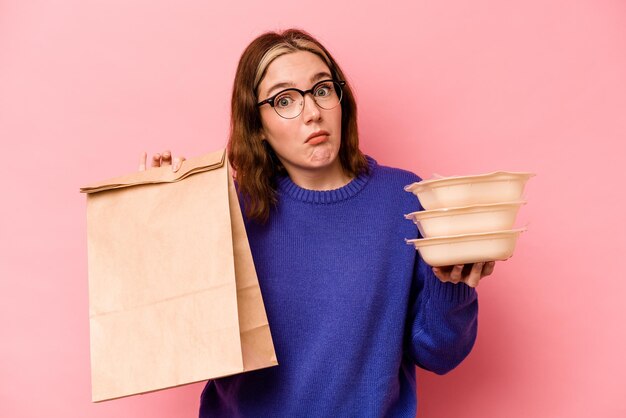 Jeune femme caucasienne tenant un tupperware et un sac à emporter isolé sur fond rose