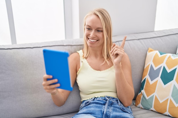 Jeune femme caucasienne utilisant un pavé tactile assis sur le canapé souriant heureux pointant avec la main et le doigt sur le côté