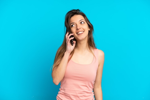 Jeune femme caucasienne utilisant un téléphone portable isolé sur fond bleu en pensant à une idée tout en levant les yeux