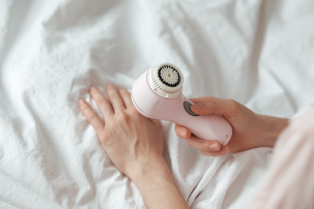 Jeune femme caucasienne utilise une brosse pour nettoyer le visage et masser.