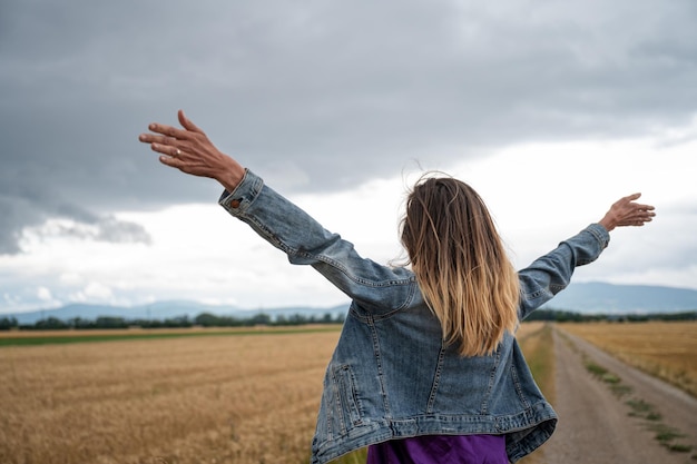 Jeune femme caucasienne en veste de jeans célébrant la vie debout avec ses bras grands ouverts