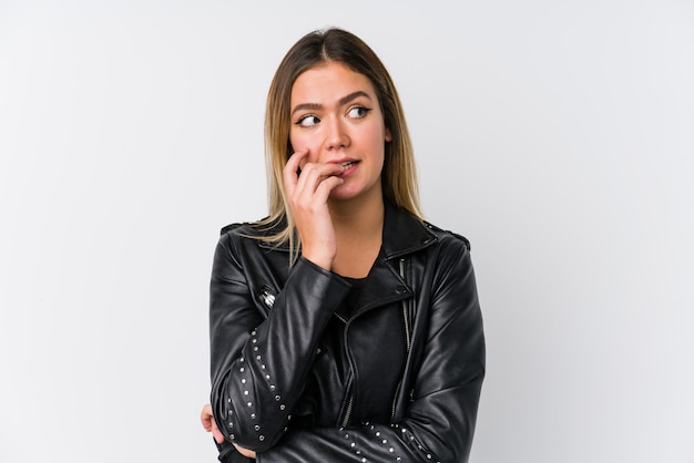 Jeune femme caucasienne vêtue d'une veste en cuir noir se mordant les ongles, nerveuse et très anxieuse.