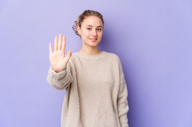 Jeune femme caucasienne sur violet souriant joyeux montrant le numéro cinq avec les doigts.