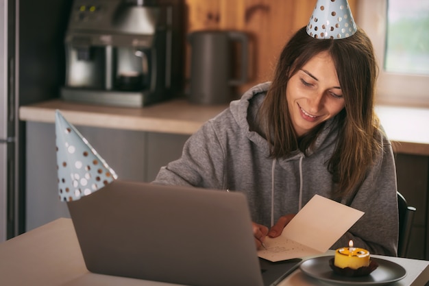 Jeune femme célébrant son anniversaire à la maison avec des amis sur appel vidéo