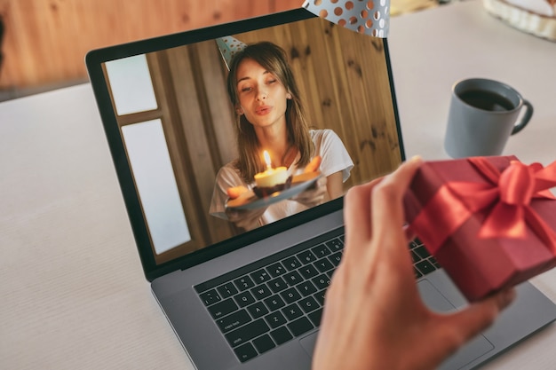 Jeune femme célébrant son anniversaire à la maison avec des amis sur appel vidéo