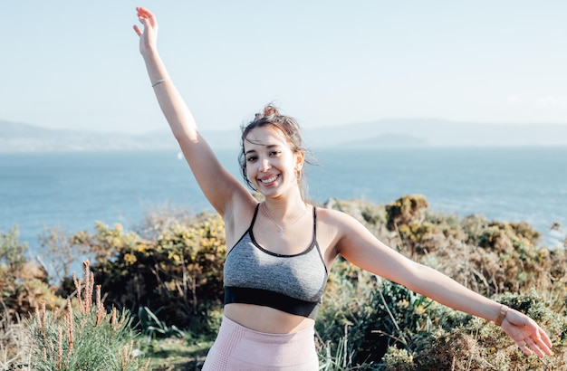 Jeune femme célèbre la fin d'une séance d'exercices en plein air sur le littoral Danser et lever les bras en l'air Heureux jeunes s'entraînant pendant une journée d'été ensoleillée se préparant pour le corps de la plage