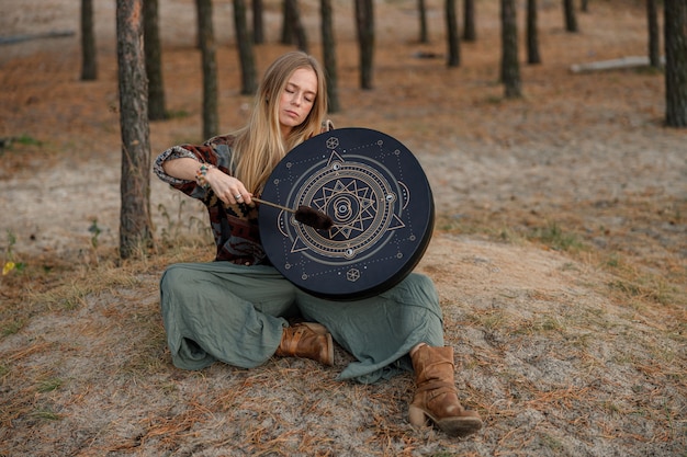 Une jeune femme chamane ethnique mature marche et joue de la musique méditative à la batterie