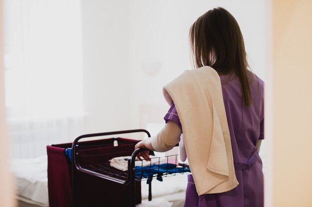 Jeune femme de chambre poussant le chariot pendant le nettoyage des chambres d'hôtel