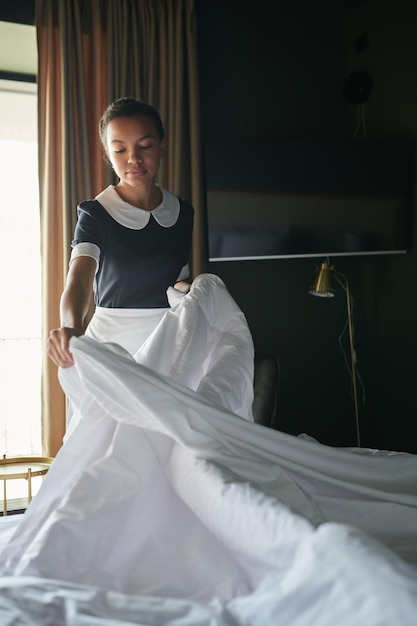 Jeune femme de chambre en uniforme debout près d'un lit double et d'une couverture à langer