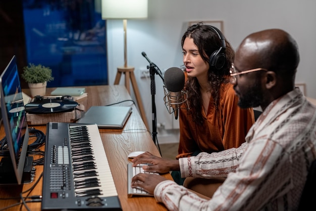 Jeune femme chantant dans un microphone tandis qu'un homme noir enregistrait ses chansons