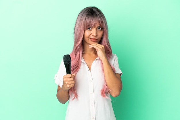 Jeune femme chanteuse métisse aux cheveux roses isolée sur fond vert pensant