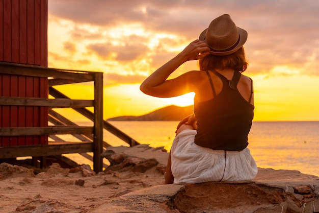 Jeune femme avec chapeau au coucher du soleil sur la plage de Cala Comte sur l'île d'Ibiza Baléares