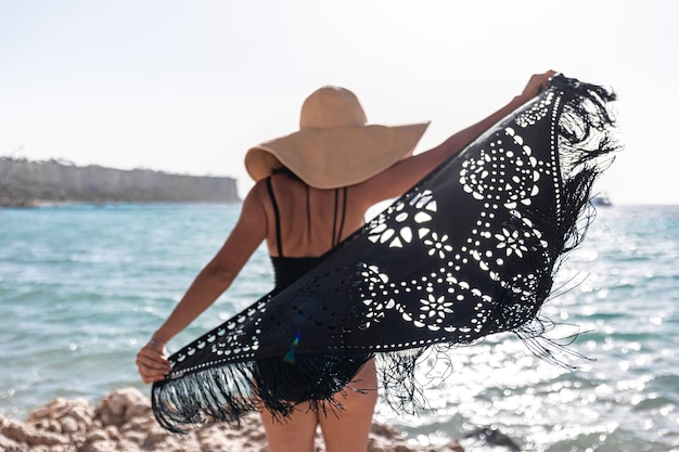 Une jeune femme avec un chapeau et une cape se repose près de la mer.