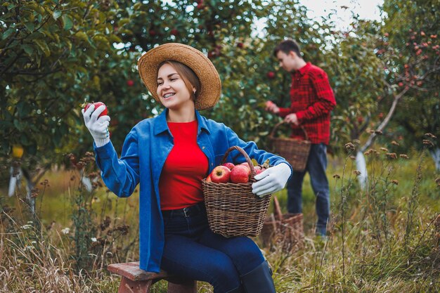 Une jeune femme avec un chapeau dans un verger de pommes Des femmes avec des chapeaux rassemblent des pommes rouges dans un panier sur le fond de la nature Récoltent des pommes dans le jardin La saison d'automne dans le verger