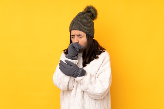 Jeune femme avec chapeau d'hiver sur fond jaune isolé souffre de toux et de malaise