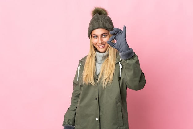 Jeune femme avec chapeau d'hiver isolé montrant signe ok avec les doigts