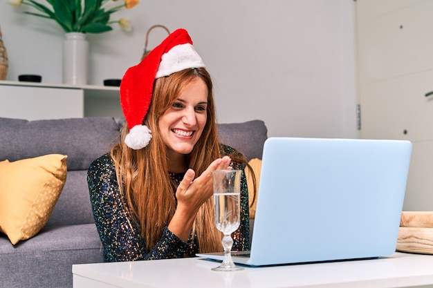 Jeune femme avec chapeau de père Noël faisant un appel vidéo à sa famille pour célébrer Noël.