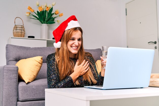 Jeune femme avec chapeau de père Noël faisant un appel vidéo à sa famille pour célébrer Noël.