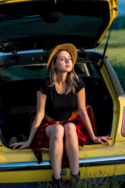 Jeune femme avec chapeau se trouve dans le coffre de la voiture en campagne