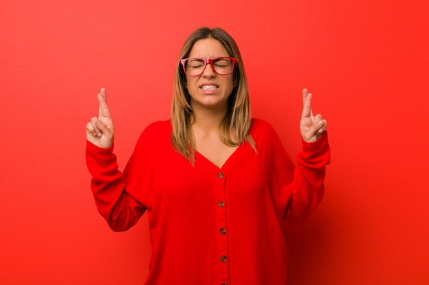 Jeune femme charismatique authentique contre un mur traversant les doigts pour avoir de la chance