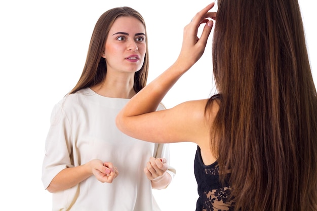 Jeune femme charmante en chemise blanche parlant à une autre sur fond blanc en studio