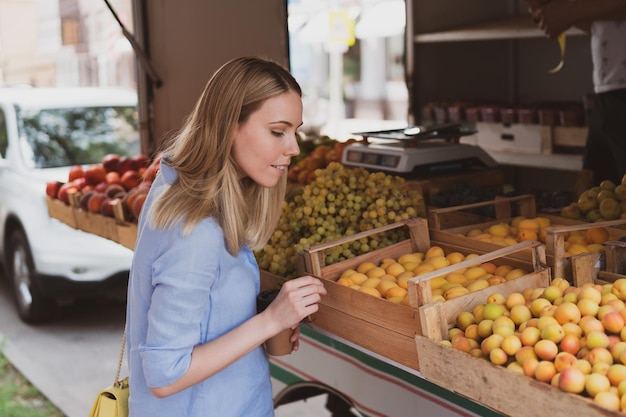 La jeune femme charmante choisit des fruits au magasin de rue
