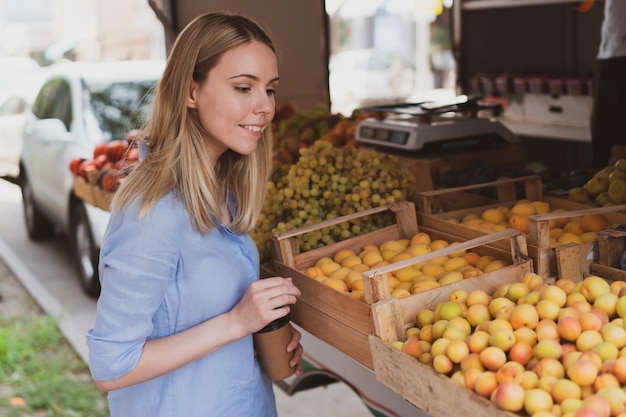 La jeune femme charmante choisit des fruits au magasin de rue