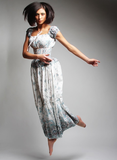 Jeune femme charmante en robe de mousseline sautant par-dessus le backgro gris