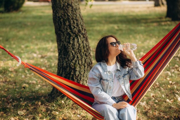 Une jeune femme charmante se détend sur un hamac et boit de l'eau froide avec de la menthe et du citron Photo de haute qualité