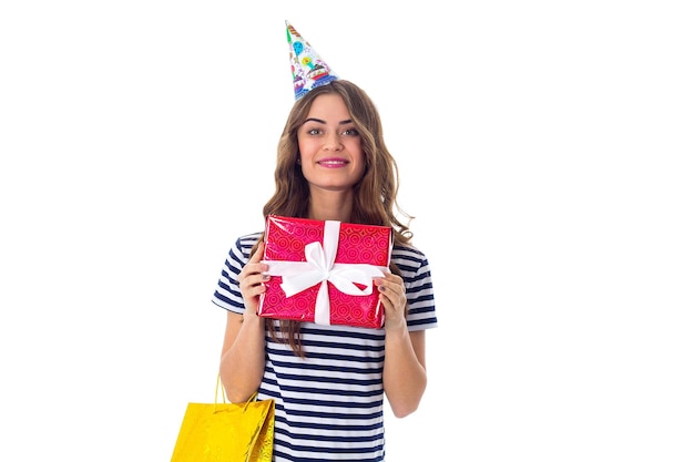 Jeune femme charmante en T-shirt dépouillé et casquette de célébration montrant des cadeaux sur fond blanc en studio
