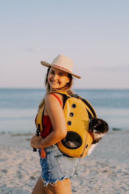 jeune femme avec un chat dans un sac à dos au bord de la mer. Concept de voyage avec un animal de compagnie. Chat dans le sac à dos avec hublot.