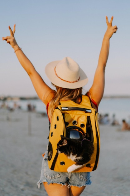 jeune femme avec un chat dans un sac à dos au bord de la mer. Concept de voyage avec un animal de compagnie. Chat dans le sac à dos avec hublot.