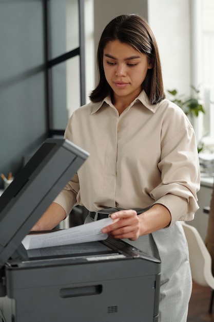Jeune femme chef de bureau debout près d'une machine Xerox lors de la copie d'un document