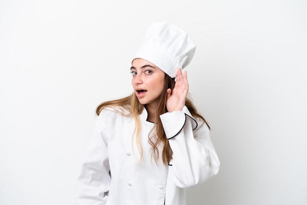 Jeune femme chef caucasienne isolée sur fond blanc écoutant quelque chose en mettant la main sur l'oreille