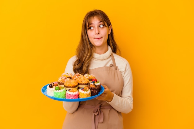 Jeune Femme Chef Pâtissier Isolée Sur Fond Jaune Confuse, Se Sent Douteuse Et Incertaine.