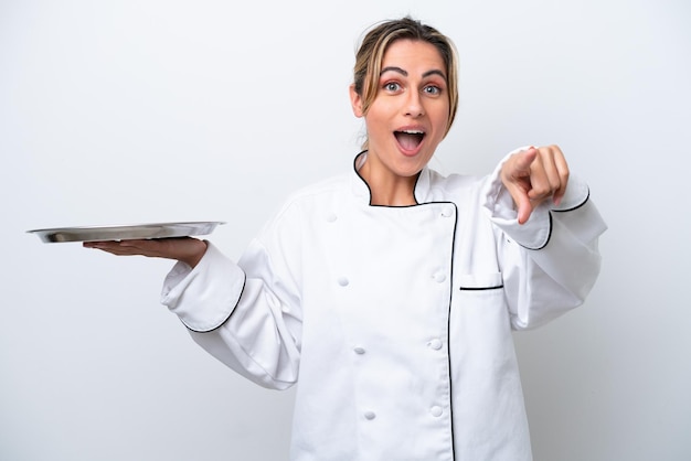 Jeune femme chef avec plateau isolé sur fond blanc surpris et pointant vers l'avant