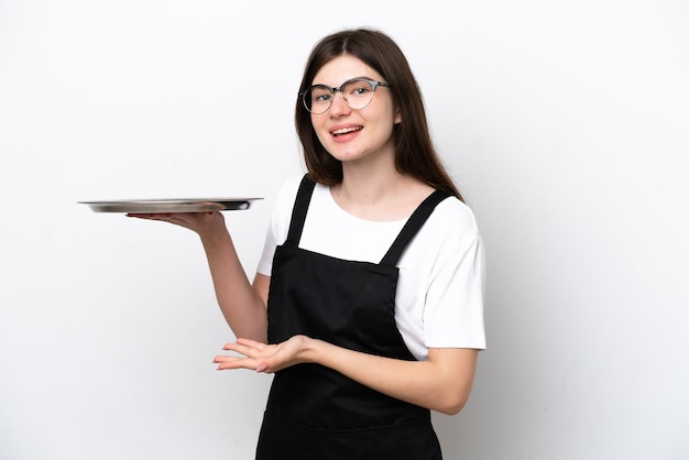 Jeune femme chef russe avec plateau isolé sur fond blanc tendant les mains sur le côté pour inviter à venir