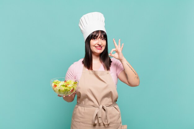 Jeune femme chef se sentant heureuse, détendue et satisfaite, montrant son approbation avec un geste correct, souriant