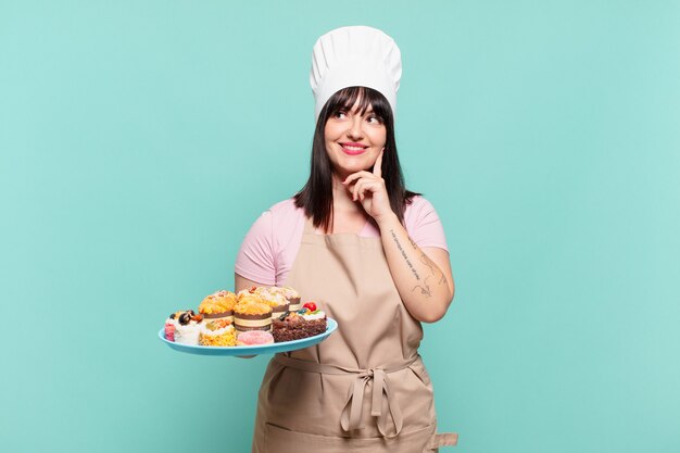 Jeune femme chef souriante joyeusement et rêvant ou doutant, regardant sur le côté