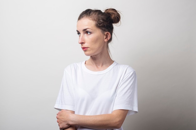 Jeune femme en chemise blanche détourne le regard sur un fond clair.