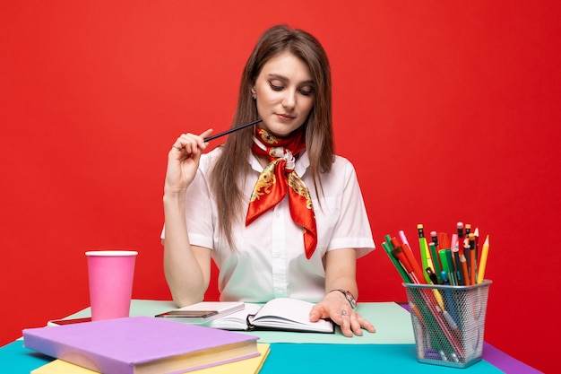 Une jeune femme en chemise blanche travaille à un bureau sur un mur rouge