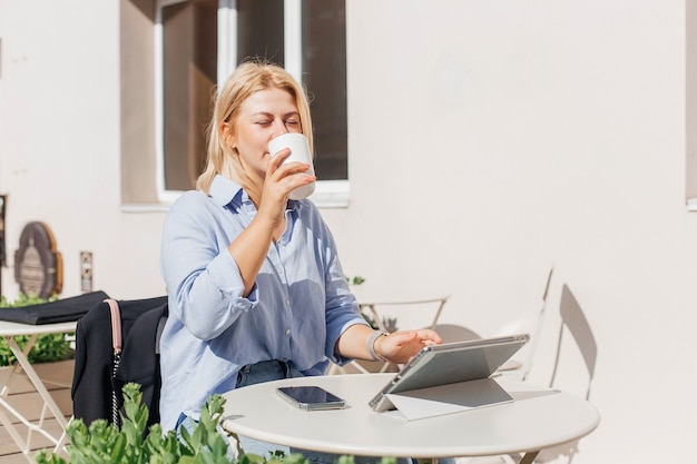 Jeune femme en chemise bleue travaillant sur un ordinateur portable dans un café et buvant du café
