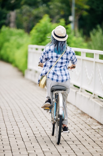 Photo jeune femme en chemise à carreaux et chapeau seau à vélo, vue de l'arrière