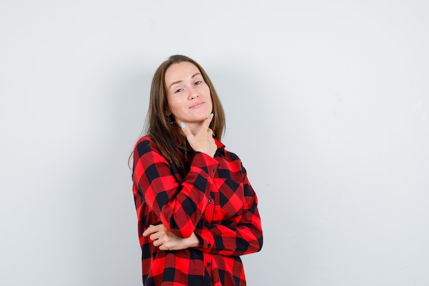 Jeune femme en chemise à carreaux s'appuyant sur le menton et à la charmante, vue de face.