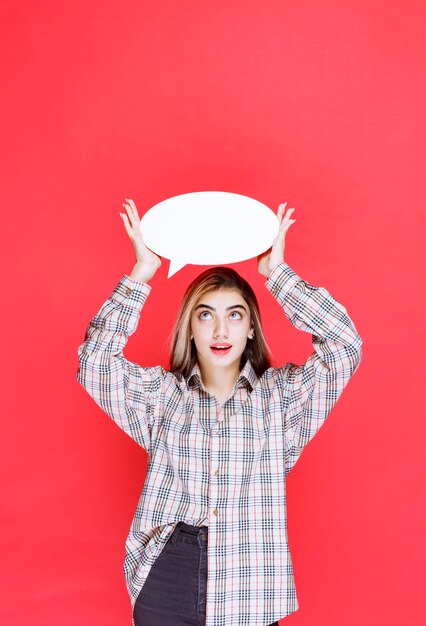 Jeune femme en chemise à carreaux tenant un panneau d'information ovale