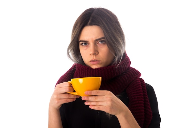 Jeune femme en chemise noire avec foulard vineux tenant une tasse jaune sur fond blanc en studio