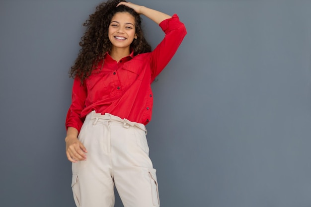 Jeune femme en chemise rouge debout contre un mur gris