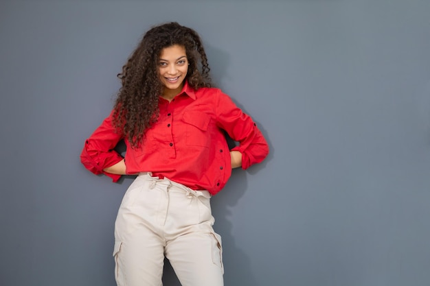 Jeune femme en chemise rouge debout contre un mur gris