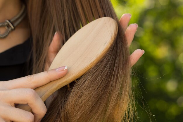 Jeune femme en chemisier et collier en argent peignant ses longs cheveux sur le fond des arbres verts